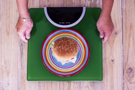 Frau betrachtet Hamburger auf grüner Gewichtswaage - gesundes und gesundes Lebensstilkonzept 