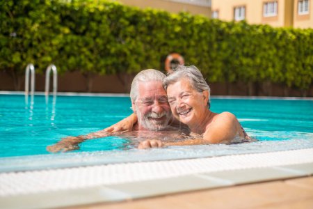 Couple of two happy seniors having fun and enjoying together in the swimming pool smiling and playing. Happy people enjoying summer outdoor in the water 