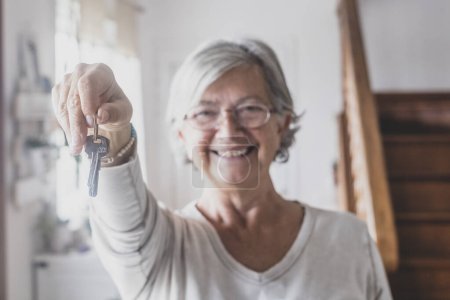 Portrait of happy senior woman holding keys of new home or property. Old lady showing or giving keys to house. Elderly female happy for moving into new apartment 