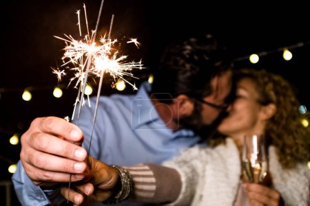 cute couple of two adults in love giving a loss together the new year night playing with sparklers in their hand near of the camera kissing each others 