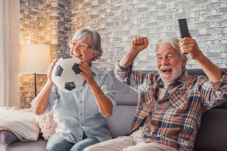 Téléchargez les photos : Joyeux couple d'aînés ou de fans de football regardant le football à la télévision et célébrant la victoire à la maison. Concept de famille, sport et divertissement. - en image libre de droit