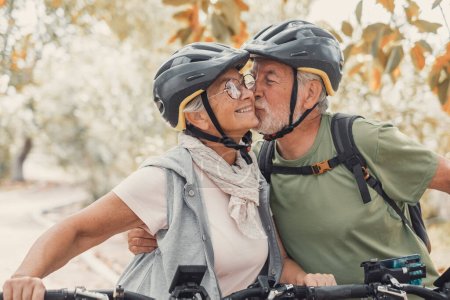 Un par de seniors lindos y dulces enamorados disfrutando juntos de la naturaleza al aire libre divirtiéndose con bicicletas. Viejo besando a su esposa sonriendo y sintiéndose bien.