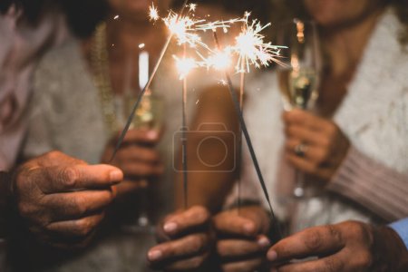 group of four people enjoying new year night celebrating with sparklers in the middle and looking at the camera - adults having fun together 