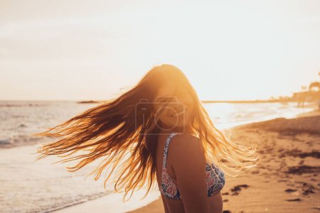 Foto de Una joven mujer caucásica mirando a la cámara sonriendo y divirtiéndose en la playa. Mujer adolescente disfrutando de la puesta de sol al aire libre. - Imagen libre de derechos