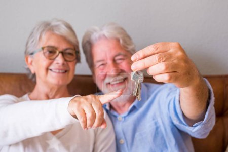 Close up of senior couple showing keys of house. Elderly couple holding keys for investment of property concept. Satisfied old couple holding keys to their new house  