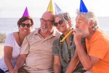 Gruppe von vier alten und reifen Freunden, die zusammen am Strand eine Party oder ein Ereignis feiern. Senioren haben Spaß und genießen Geburtstag 