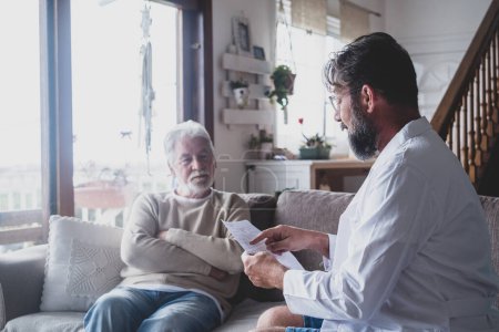 Photo for Male professional doctor consulting senior patient during medical care visit. Young man physician and old mature senior talking providing medical assistance sitting on sofa. Elderly people home care concept - Royalty Free Image