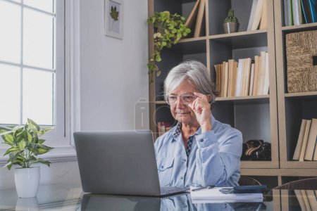 Glückliche alte kaukasische Geschäftsfrau lächelnd bei der Online-Arbeit Webinar-Podcast auf Laptop und Lernkurskonferenz Aufruf machen Notizen am Schreibtisch sitzen, E-Learning-Konzept 