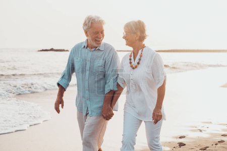 Photo for Couple of old mature people walking on the sand together and having fun on the sand of the beach enjoying and living the moment. Two cute seniors in love having fun. Barefoot walking on the water - Royalty Free Image