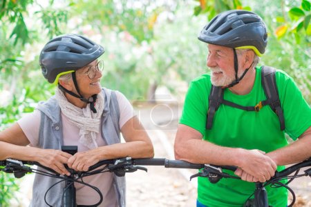 Portrait of couple of old and happy in love seniors looking each other smiling and having fun with their bikes in the nature outdoors together feeling good and healthy. 