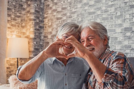 Foto de Primer plano de las manos de dos abuelos maduros haciendo una forma de corazón con los dedos juntos. Sonriendo y divirtiéndose en el amor personas. - Imagen libre de derechos