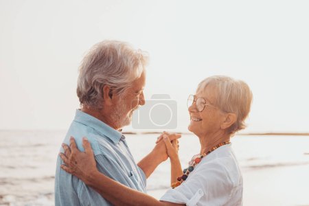 Téléchargez les photos : Couple de vieilles personnes mûres dansant ensemble et s'amusant sur le sable à la plage profiter et vivre l'instant. Portrait de personnes âgées amoureuses qui se regardent en s'amusant. - en image libre de droit