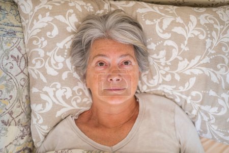 Photo for Senior insomaniac woman lying awake in bed looking up and trying to sleep. Top view of unhappy old lady feeling disturbed suffering from insomnia. Depressed female having problem lying down in bedroom at home - Royalty Free Image