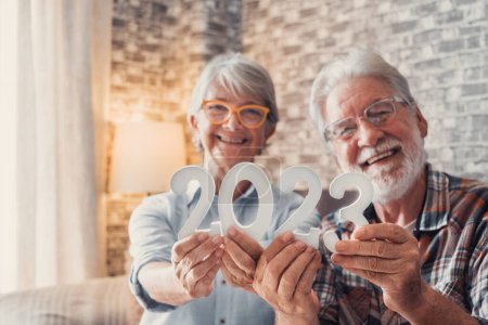 Portrait of couple of two old pensioners holding together numbers of 2023 at home. Close up of new year numbers, celebrating and goals for new life concept. 