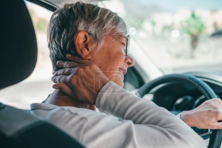 Photo for Rear view of old woman having neck pain while driving a car. One senior or mature people feeling bad for injury. - Royalty Free Image