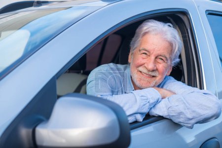 Happy owner looking at the camera with happy face. Handsome bearded mature man sitting relaxed in his newly bought car looking out the window smiling joyfully. One old senior driving and having fun.