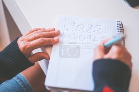 Photo for Planning, motivation for the new year 2022. Hands of old woman writing new year 2022 goals in diary. Word writing text 2022 Goals in a notebook. Business or personal goals for new year - Royalty Free Image