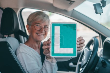 Téléchargez les photos : Une vieille femme obtient le laissez-passer pour conduire une voiture à un âge mûr. Senior regardant vers le permis L dans le siège d'entraînement célébrant le succès - en image libre de droit