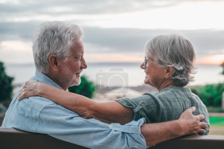 Foto de Head shot close up portrait happy grey haired middle aged woman snuggling to smiling older husband, enjoying sitting on bench at park. Bonding loving old family couple embracing, looking sunset. - Imagen libre de derechos