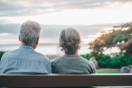 Foto de Head shot close up portrait happy grey haired middle aged woman with older husband, enjoying sitting on bench at park. Bonding loving old family couple embracing, looking sunset. - Imagen libre de derechos
