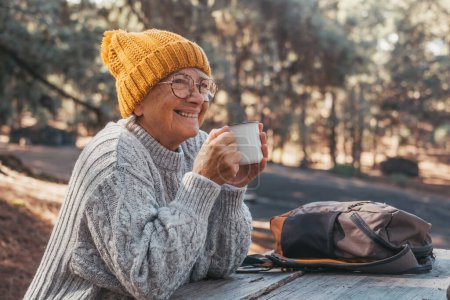 Photo for Head shot portrait close up of middle age woman relaxing drinking coffee or tea sitting at table in the forest of mountain in the middle of nature. Autumn season enjoying concept lifestyle. - Royalty Free Image
