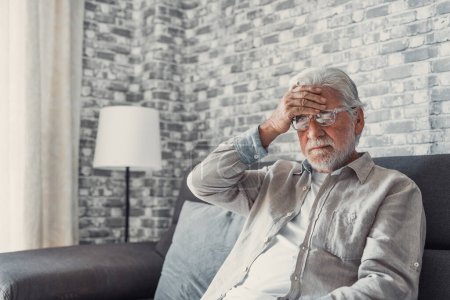 Photo for Frustrated unhealthy senior mature man touching head, having painful feelings sitting alone at home. Unhappy middle aged retired grandfather suffering from high blood pressure disease indoors. - Royalty Free Image