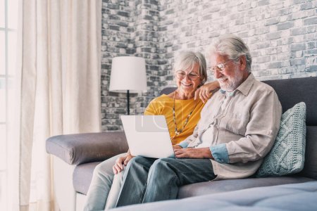 Photo for Pretty elderly 70s grey-haired couple resting on couch in living room hold on lap laptop watching movie smiling enjoy free time, older generation and modern wireless technology advanced users concept - Royalty Free Image
