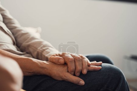 Close up elderly affectionate woman covering wrinkled hands of mature husband, showing love and support at home. Caring middle aged family couple enjoying sincere trustful honest conversation.