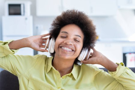 Portrait and close up of one happy and cheerful afro American young woman enjoying and having fun listening music and singing songs at home on the sofa. Carefree lifestyle concept.