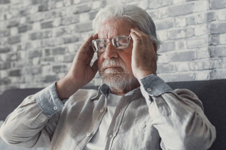 Frustrado anciano insalubre hombre maduro tocando la cabeza, teniendo sentimientos dolorosos sentado solo en casa. Infeliz abuelo jubilado de mediana edad que sufre de la enfermedad de la presión arterial alta en el interior
.