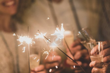 Foto de Grupo de cuatro personas divirtiéndose y disfrutando sosteniendo copas de champán y bengalas celebrando el feliz año nuevo juntos - Imagen libre de derechos