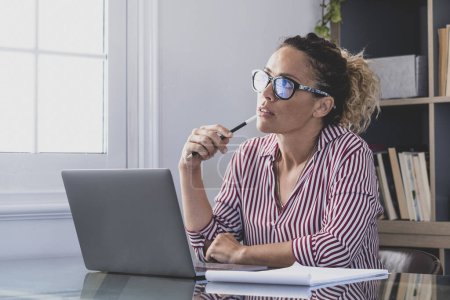 Réflexion caucasienne regardant l'écran d'ordinateur portable, réfléchissant sur le travail, femme d'affaires indépendante travaillant dans un projet difficile. Femme se préparant à la maison dans le bureau intérieur.