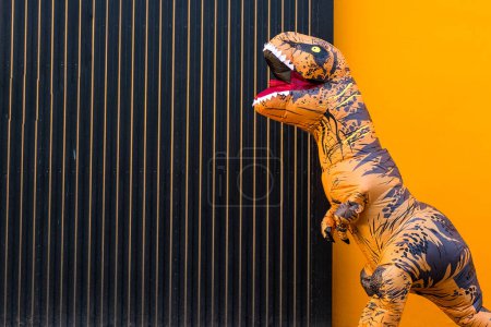 One happy and funny dinosaur costume dancing in the street with a orange colorful background - t-rex having fun - funny man inside of a costume of dino