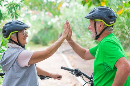 Téléchargez les photos : Couple de deux personnes âgées donnant cinq ensemble à l'extérieur en s'amusant avec des vélos profitant de la nature. Couple de personnes âgées construisant un mode de vie sain et en forme. - en image libre de droit