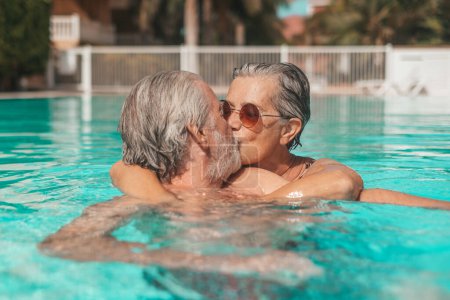 Téléchargez les photos : Couple de deux aînés heureux s'amuser et profiter ensemble dans la piscine souriant et jouer. Des gens heureux profitant de l'été en plein air dans l'eau - en image libre de droit