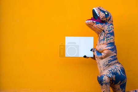 One happy and funny dinosaur costume dancing in the street with a orange colorful background - t-rex having fun - funny man inside of a costume of dino