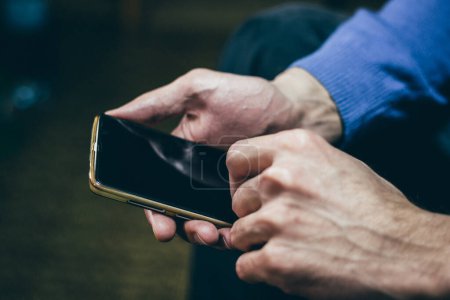 Téléchargez les photos : Man holding and using a smartphone with both hands. Close up, dark tone, blurred background. - en image libre de droit