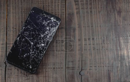 Téléchargez les photos : Smartphone mobile avec écran tactile cassé sur une vieille table en bois. LCD avec de nombreuses fissures et de petits morceaux de verre. Copier l'espace vide, vue du dessus, concept de réparation de téléphone. - en image libre de droit