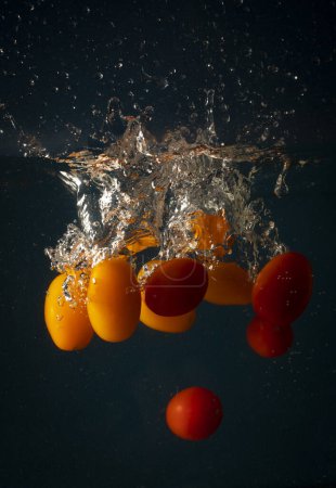 Foto de Tomates cherry que caen en el agua causando salpicaduras. Concepto de frescura y buena salud a través de la nutrición - Imagen libre de derechos