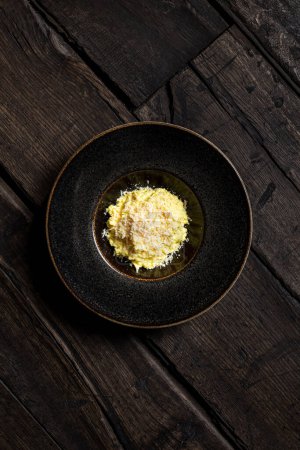 Téléchargez les photos : Porridge de maïs Mamaliga au fromage de chèvre et morceaux de bacon de porc dans une assiette en céramique sombre avec de larges marges sur des planches en bois foncé. - en image libre de droit