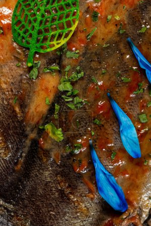 Téléchargez les photos : Truite de rivière grillée à la tomate et sauce aux légumes à l'ail. Le poisson repose sur une plaque de verre transparente sur un fond clair de blocs de bois. - en image libre de droit