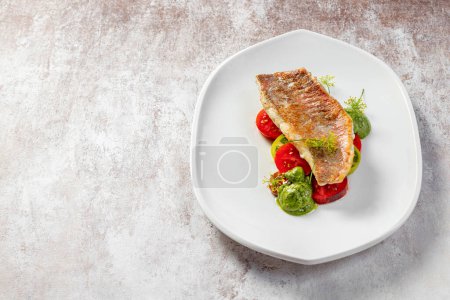Photo for Grilled sea bass fillet with green and red tomatoes and pesto sauce. Food lies on a light ceramic plate on a light background. - Royalty Free Image