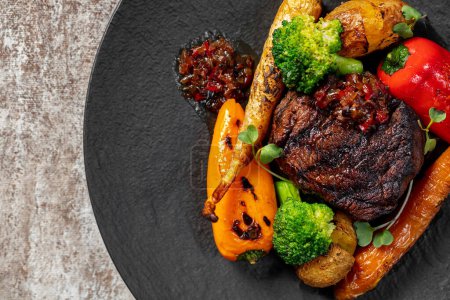 Photo for Grilled filet mignon steak with vegetables carrots, paprika broccoli in cherry sauce. Food lies on a dark slate plate on a light background. - Royalty Free Image