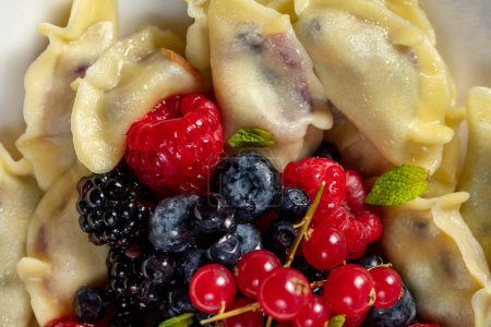 Photo for Cherry dumplings decorated with blackberries, blueberries, raspberries and red currants in a light ceramic plate on a light background. - Royalty Free Image