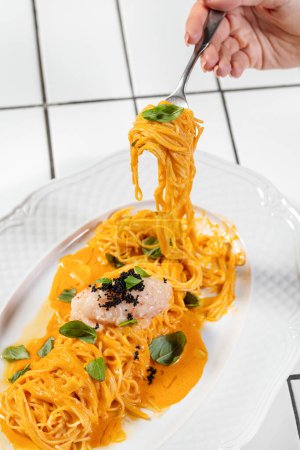 Photo for Spaghetti with cheese sauce and scallop tartare with finely chopped onion and black caviar on a light ceramic plate. The plate stands on a light background. - Royalty Free Image