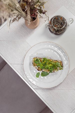 Photo for Forshmak of herring on buckwheat toast with pickled grapes, mint leaves and cilantro. Food lies on a light ceramic plate. The plate stands on a light background. - Royalty Free Image