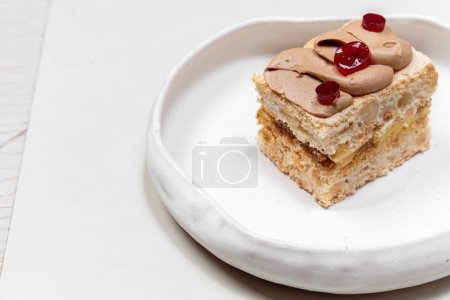 Photo for Kyiv cake with hazelnuts, bizet, chocolate cream and pickled cherries on top. A piece of cake lies on a light ceramic plate on a light background. - Royalty Free Image