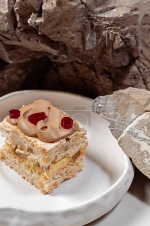 Téléchargez les photos : Gâteau de Kiev avec noisettes, bizet, crème au chocolat et cerises marinées sur le dessus. Un morceau de gâteau repose sur une plaque de céramique légère sur un fond clair. - en image libre de droit