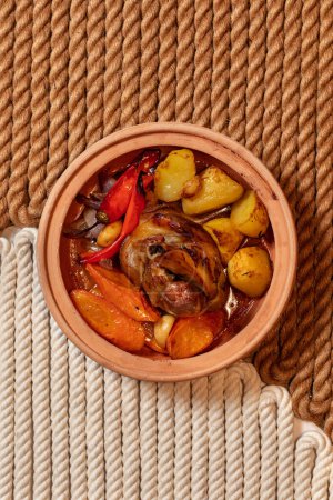 Foto de Pierna de cordero al horno con patatas, pimentón, zanahorias y cebollas rojas en un plato de cerámica con tapa. - Imagen libre de derechos