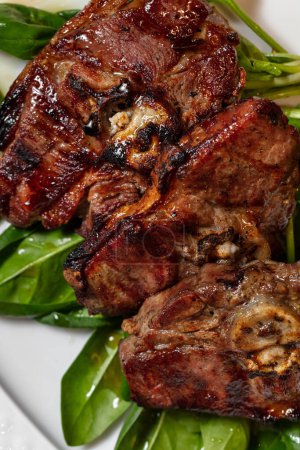 Téléchargez les photos : Steak de porc sur l'os grillé avec de la laitue. La nourriture repose sur une assiette légère et ovale. - en image libre de droit